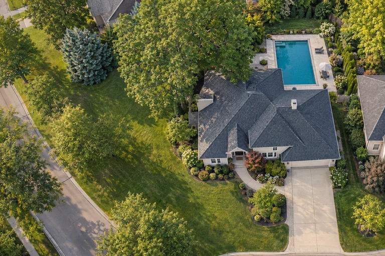 Illustrative aerial view of a home with a pool, planting beds and mature trees